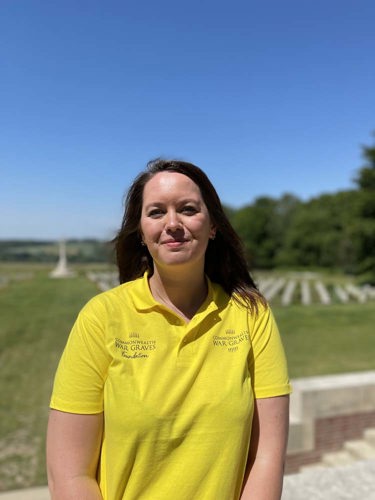 Estelle poses in a yellow CWGF polo shirt in front of the graves at the Thiepval Memorial